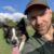 Homme et chien souriants dans un parc verdoyant.
