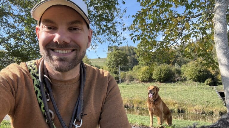 Homme souriant avec son chien dans un paysage verdoyant